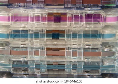 A stack of audio cassettes in close-up. You can see the magnetic tape, rollers and a pressure mechanism with a felt pad. Background image