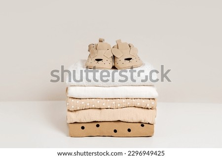 Stack of baby clothes with baby shoes. Cotton clothes and muslin swaddle blanket in pastel colors. Clean freshly laundered, neatly folded kids clothes. 