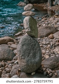 stack of balanced river rocks stands securely on the rocky shore next to beautiful clear blue-green flowing water.