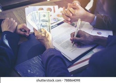 Stack of banknotes US dollars in the hands of young men. In his right hand holding a pen and signing documents on business deals by having a third party become a witness.
