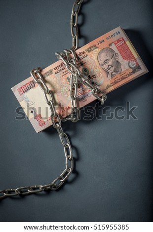 A stack of banned one thousand rupee Indian currency notes wrapped with steel chain. A concept.