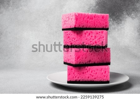 A stack of barbie pink dishwashing sponges on a white plate close-up on a neutral gray background. Gentle dishwashing. House cleaning