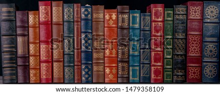 A stack of beautiful leather bound books with golden decoration against a black background.
