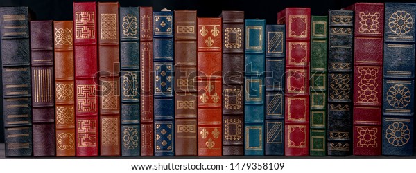 A stack of beautiful leather\
bound books with golden decoration against a black\
background.