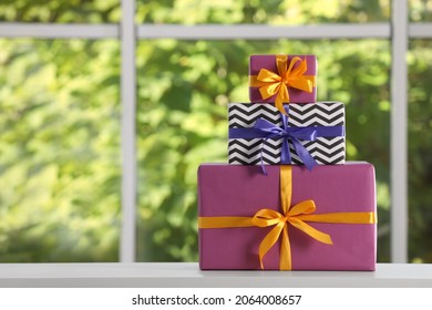 Stack of beautifully wrapped gift boxes on white table  near window. Space for text