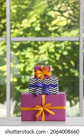 Stack of beautifully wrapped gift boxes on white table  near window. Space for text
