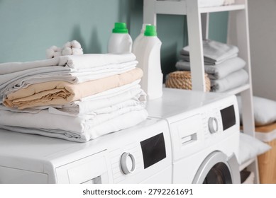 Stack of bed sheets with cotton flowers and laundry detergents on washing machines in room