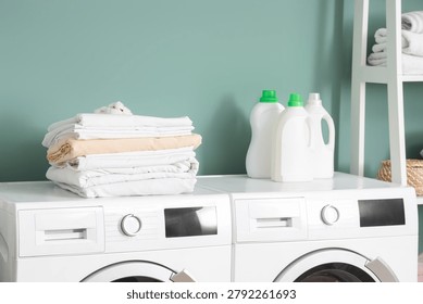 Stack of bed sheets with cotton flowers and laundry detergents on washing machines in room