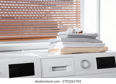 Stack of bed sheets with cotton flowers on washing machine in laundry room