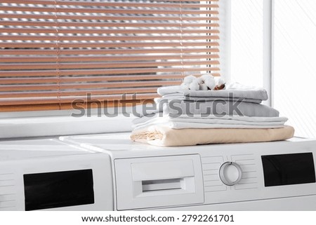 Stack of bed sheets with cotton flowers on washing machine in laundry room