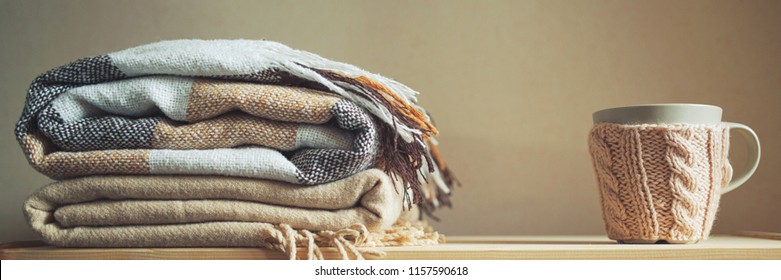 stack of beige checkered wool blankets and cup on a wooden chest. autumn - winter concept of home warmth and comfort. toned, long banner - Powered by Shutterstock