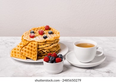 Stack of Belgian waffles, berries and cup of tea: delicious summer breakfast on marble table. Homemade waffle and mix of raspberries and blueberries as topping. Sweet dessert on white dishes - Powered by Shutterstock