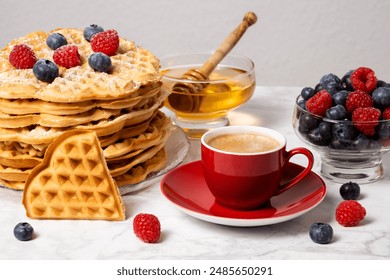 Stack of Belgian waffles, berries, honey and red cup of coffee: delicious summer breakfast on marble table. Heart-shaped waffle and mix of raspberries and blueberries as topping. - Powered by Shutterstock