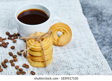 Stack of biscuits with coffee beans and a cup of coffee on a white tablecloth. High quality photo