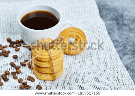 Stack of biscuits with coffee beans and a cup of coffee on a white tablecloth. High quality photo