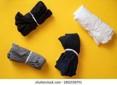 Stack Of Black, Grey And White T-shirt Rolled Up On Yellow Background