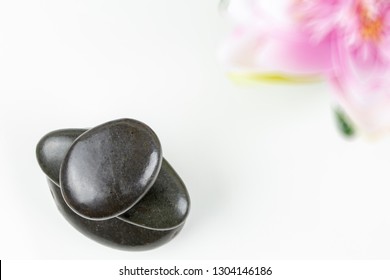 Stack of black pebbles on white background with flower. Spa Zen harmony concept