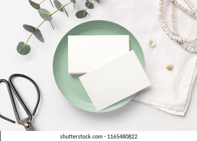 Stack Of Blank Business Cards On A White Feminine Styled Desk With Mint Bowl, Decorative Scissors, Linen Napkin And Eucalyptus Twigs. Minimalist Mock Up, Flat Lay / Top View