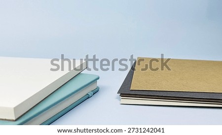 Stack of Blank Notebooks in Light Blue and White with Brown and Grey Paper on Pale Blue Background, Minimalist Stationery Set, Close-Up, Office Supplies. 