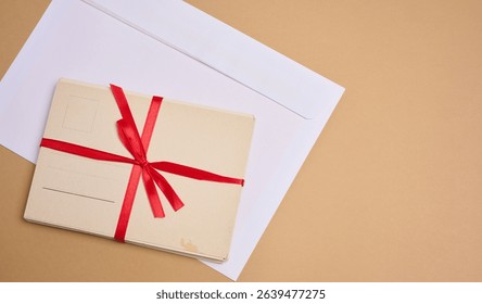 A stack of blank postcards tied with a red ribbon with a bow and an envelope lie on a beige background.