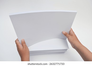 Stack of blank white paper is being held in two hands.  The top sheet is open, revealing the inside pages.