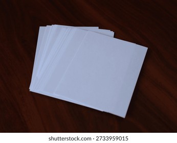 Stack of blank white paper sheets placed on a wooden table surface, showing clean edges and simple top view composition.