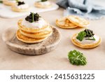 A stack of blinis pancakes with black caviar and sour cream on marble plate, close-up.