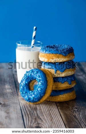 A stack of blue chocolate candy dipped donuts with a glass of milk.