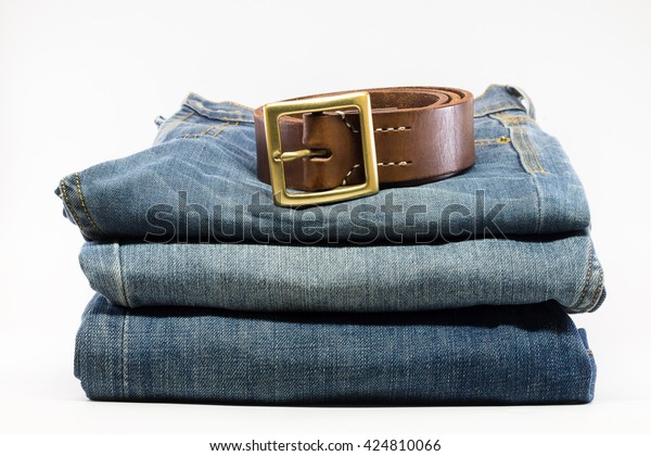 Stack of blue jeans with belt on white background.