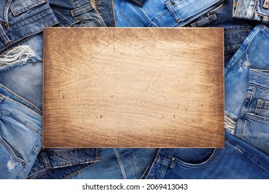 Stack Of Blue Jeans Denim And Wood Name Plate. Jeans Heap With Wooden Background Texture