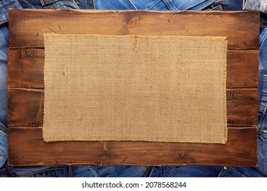 Stack Of Blue Jeans Denim And Wood Name Plate. Jeans Heap With Sack Hessian Background Texture