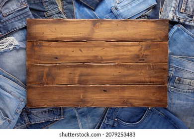 Stack Of Blue Jeans Denim And Wood Name Plate. Jeans Heap With Wooden Background Texture