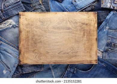 Stack Of Blue Jeans Denim And Wood Name Plate. Jeans Heap With Wooden Background Texture