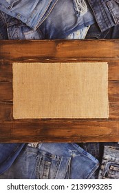 Stack Of Blue Jeans Denim And Wood Name Plate. Jeans Heap With Wooden Background Texture