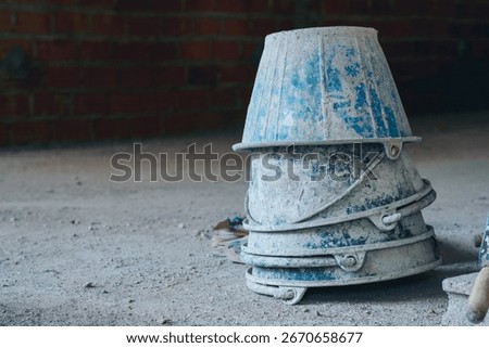 Stack of blue plastic buckets used for carrying mixed cement at a construction site, typically for bricklaying, block walls, and concrete flooring.