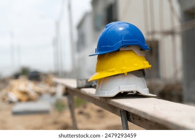 A stack of blue, yellow, and white construction hard hats on a wooden plank at a building site, indicating safety measures