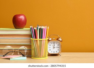 Stack of books with apple, colored pencils, glasses and alarm clock