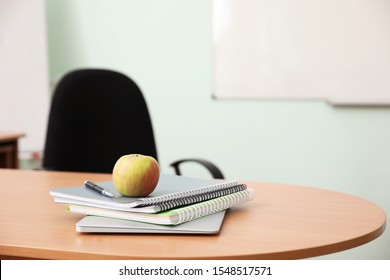 Stack Of Books, Apple And Laptop On Teacher's Desk In Classroom