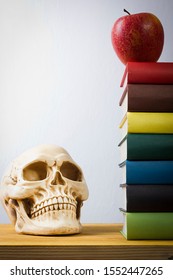 Stack of books, apple and skull on a wooden table