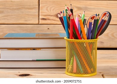 Stack of books and basket with colored pencils.