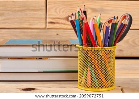 Stack of books and basket with colored pencils.