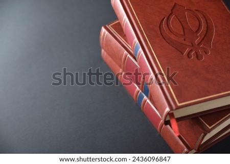 Stack of books with brown leather cover with engraved symbol of sikh culture and religion on black table. Elevated view.