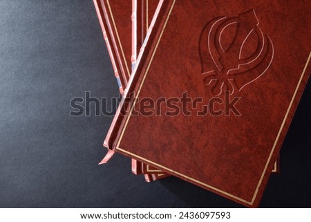 Stack of books with brown leather cover with engraved symbol of sikh culture and religion on black table. Top view.