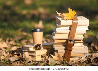 Stack of books with cup of coffee and pine cone in autumn park, closeup