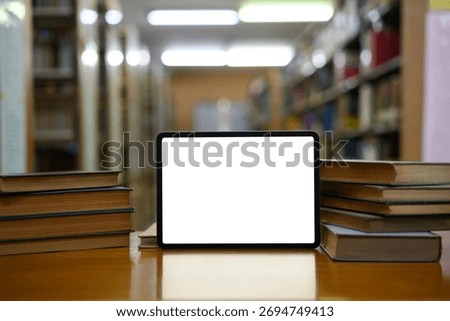 Stack of books with empty screen digital tablet in library.