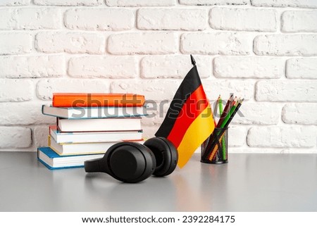 Stack of books and flag of Germany on desk. German language learning concept
