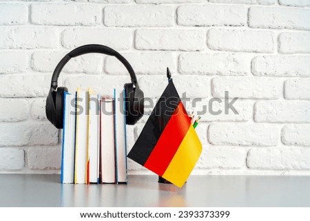Stack of books and flag of Germany on desk. German language learning concept