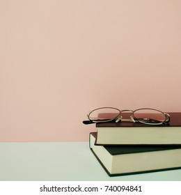 Stack of books in front of pale pink pastel background. Minimal lifestyle composition with copy space