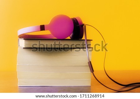 Stack of books and headphones over yellow background. Remote education concept
