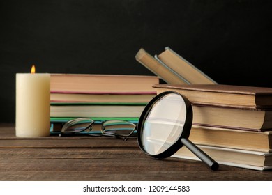 A stack of books and a magnifier on a brown wooden table and on a black background. Old books. Education. school. study